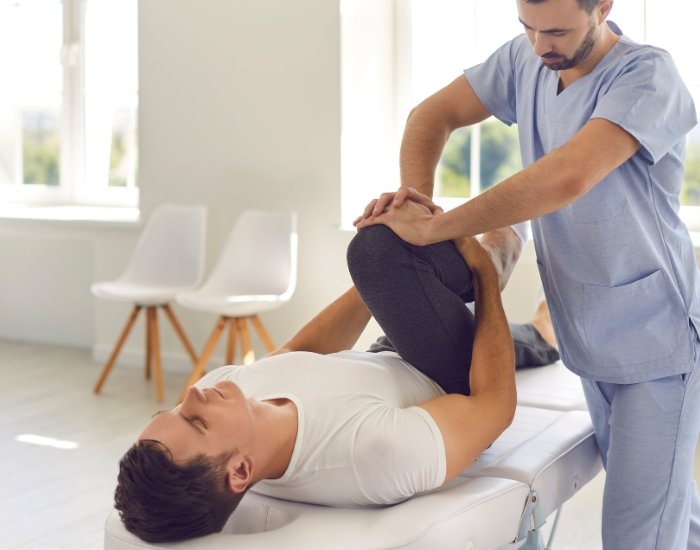 Clinician examining a patient’s hip and leg on an exam table Clinician examining a patient’s hip and leg on an exam table