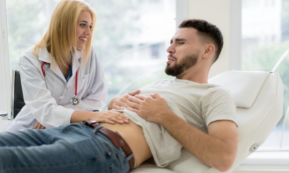 Adult experiencing abdominal pain while holding the lower abdomen during a primary care medical evaluation